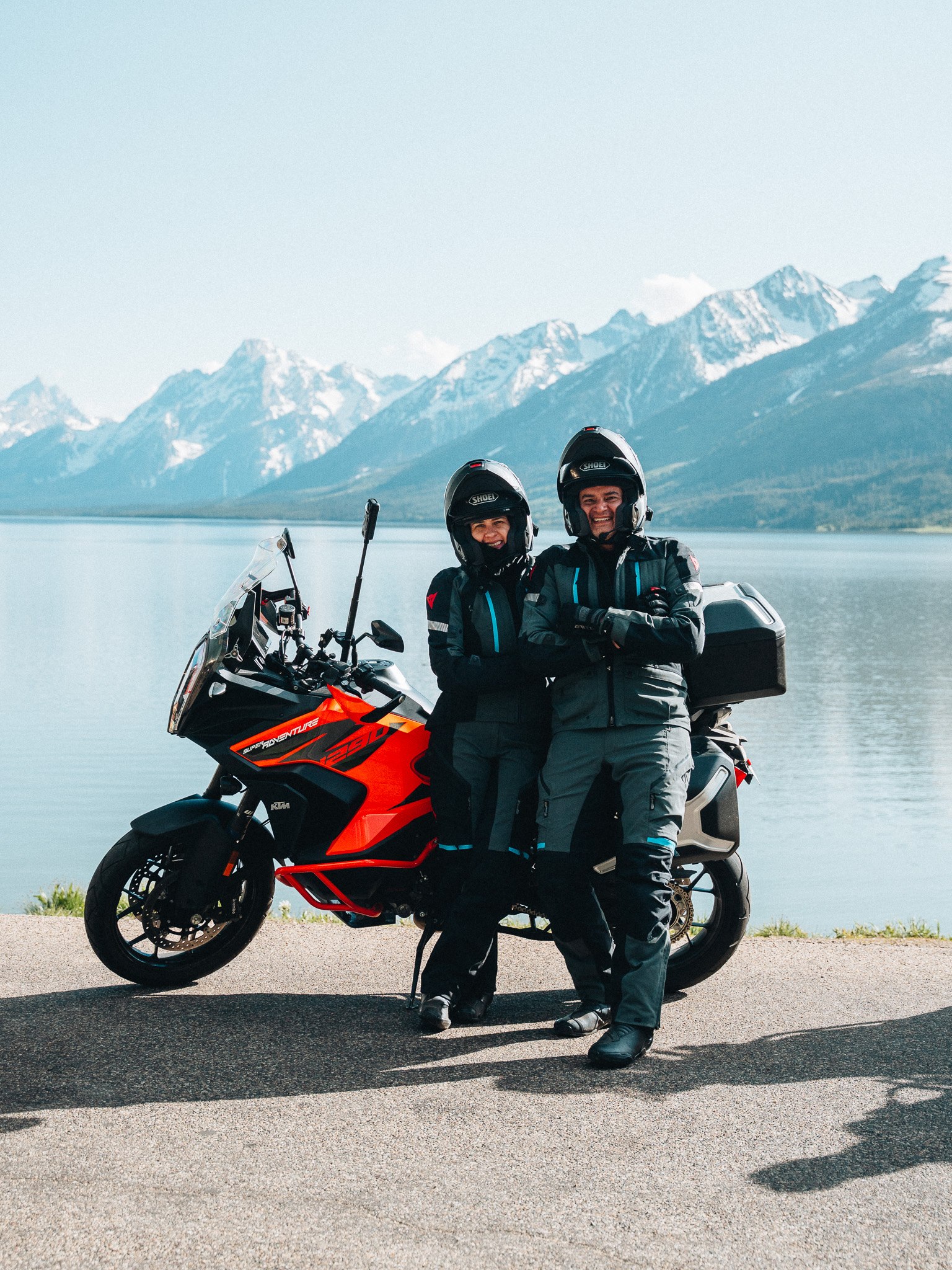 Two riders beside a lake with the Tetons behind them